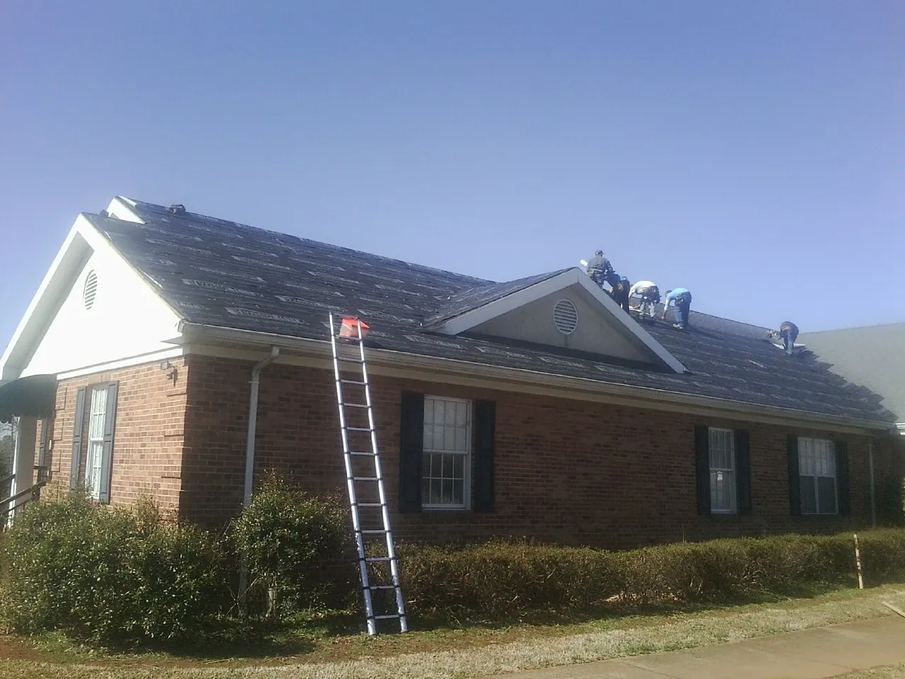 Crew tearing shingles off a brick ranch roof with a ladder set — Metal Roof Repair work by our crew in Haverhill