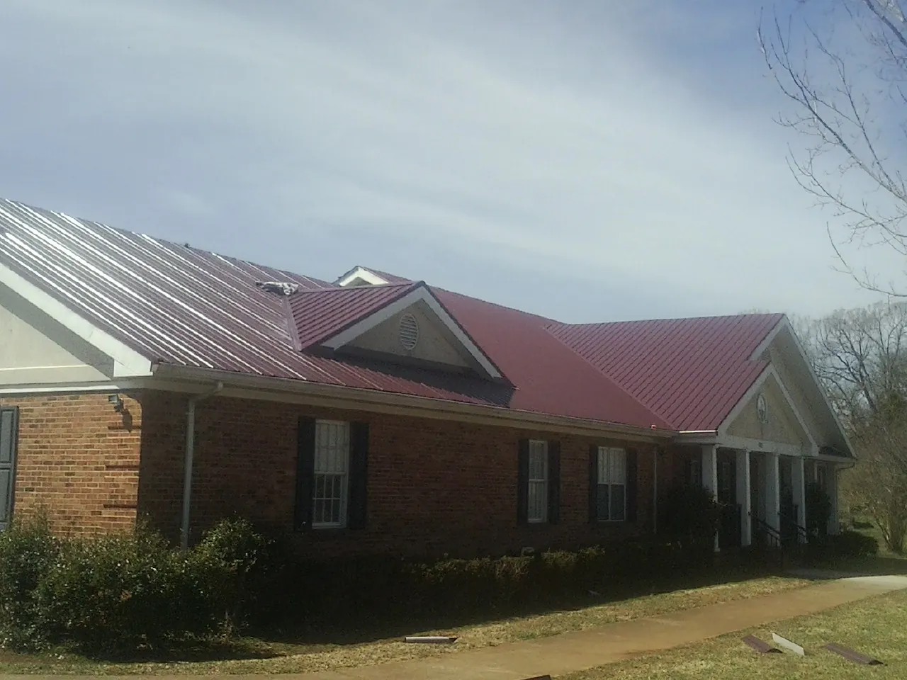 Red metal roof with gabled entries on a long brick building, from a Hail Damage Roof Repair job in Haverhill