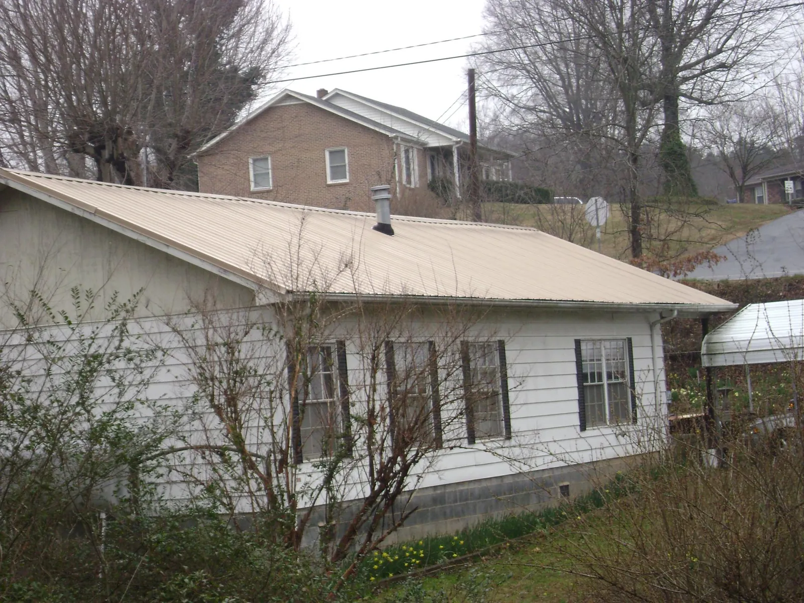 Tan metal roof on a white sided house set into a hillside — Commercial Roofing by Roofing Brothers in Haverhill